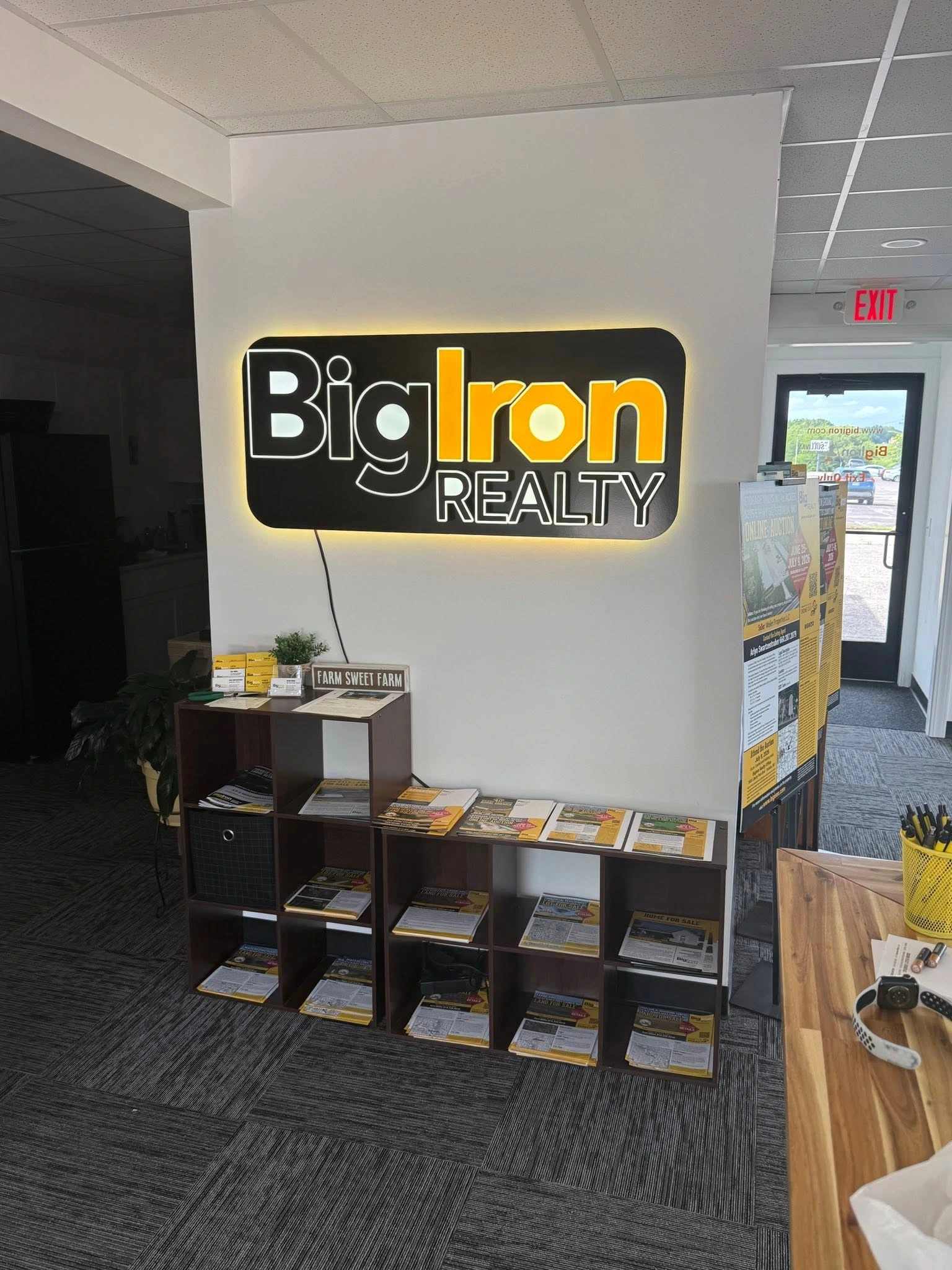 Big Iron Realty illuminated wall sign installed above office literature racks
